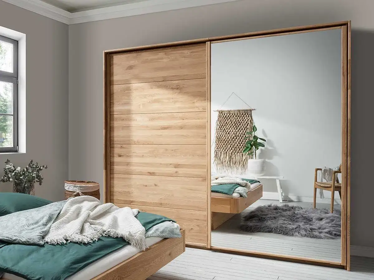 Holzschrank mit Spiegeltür, eine tolle Idee für Ihr Ankleidezimmer. Ein Bett mit grüner Bettwäsche und Decken steht daneben.