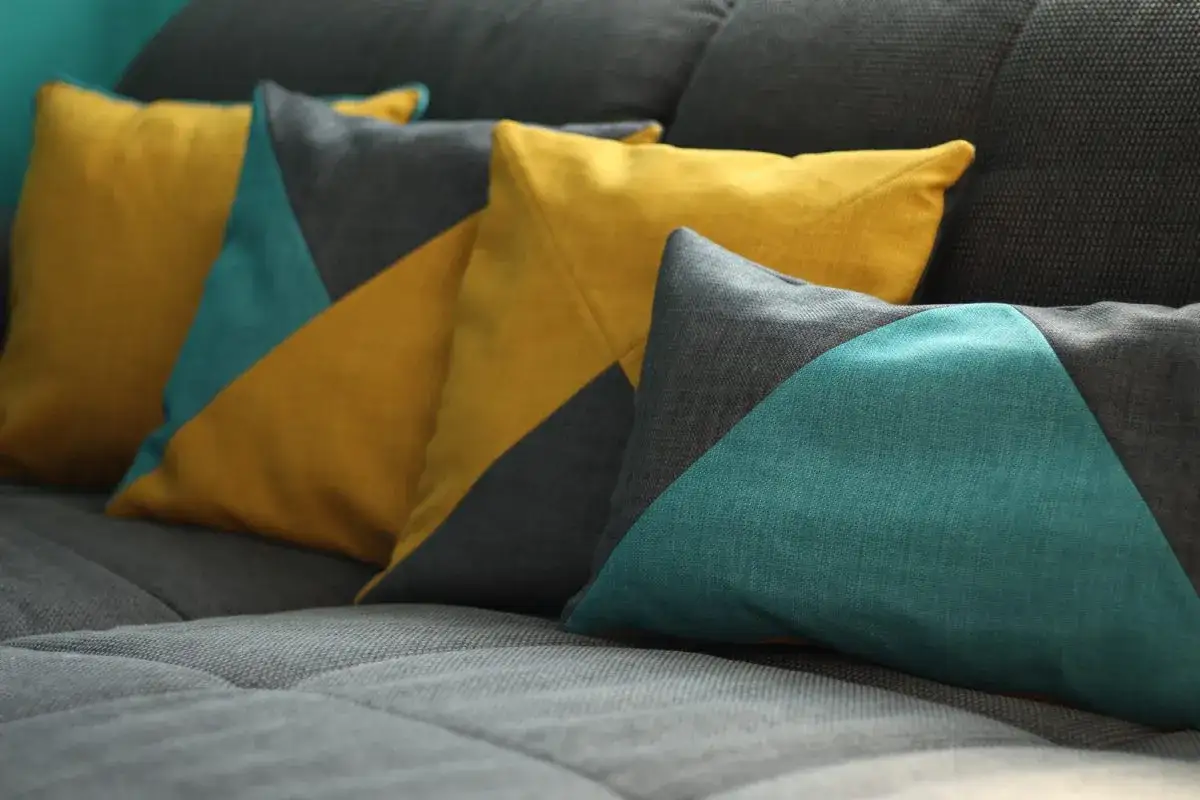 Kissen mit geometrischem Schnittmuster in Gelb, Türkis und Grau auf einem grauen Sofa.