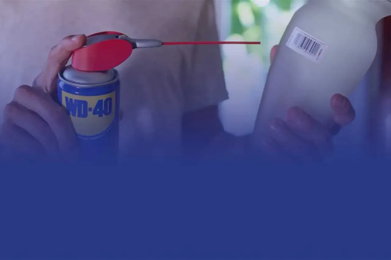 WD-40 Dose mit rotem Sprühaufsatz wird auf ein Glas mit Etikett gehalten. So lässt sich ein Aufkleber von Glas entfernen.