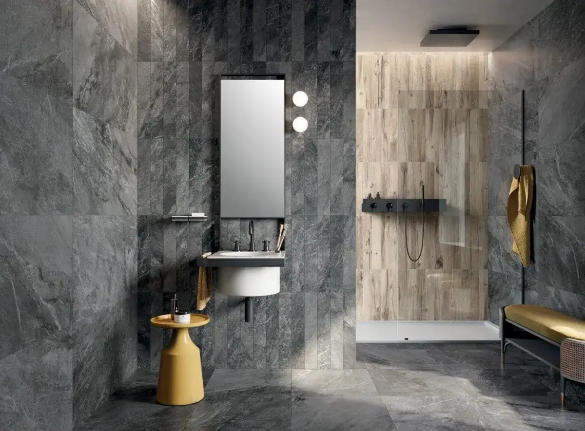 Modernes Bad mit grauen Marmorfliesen und Holzakzenten. Ein gelber Beistelltisch sorgt für einen Farbtupfer. Eine Dusche mit Holzwand und schwarzer Armatur. Bad-Inspo, die polarisiert.