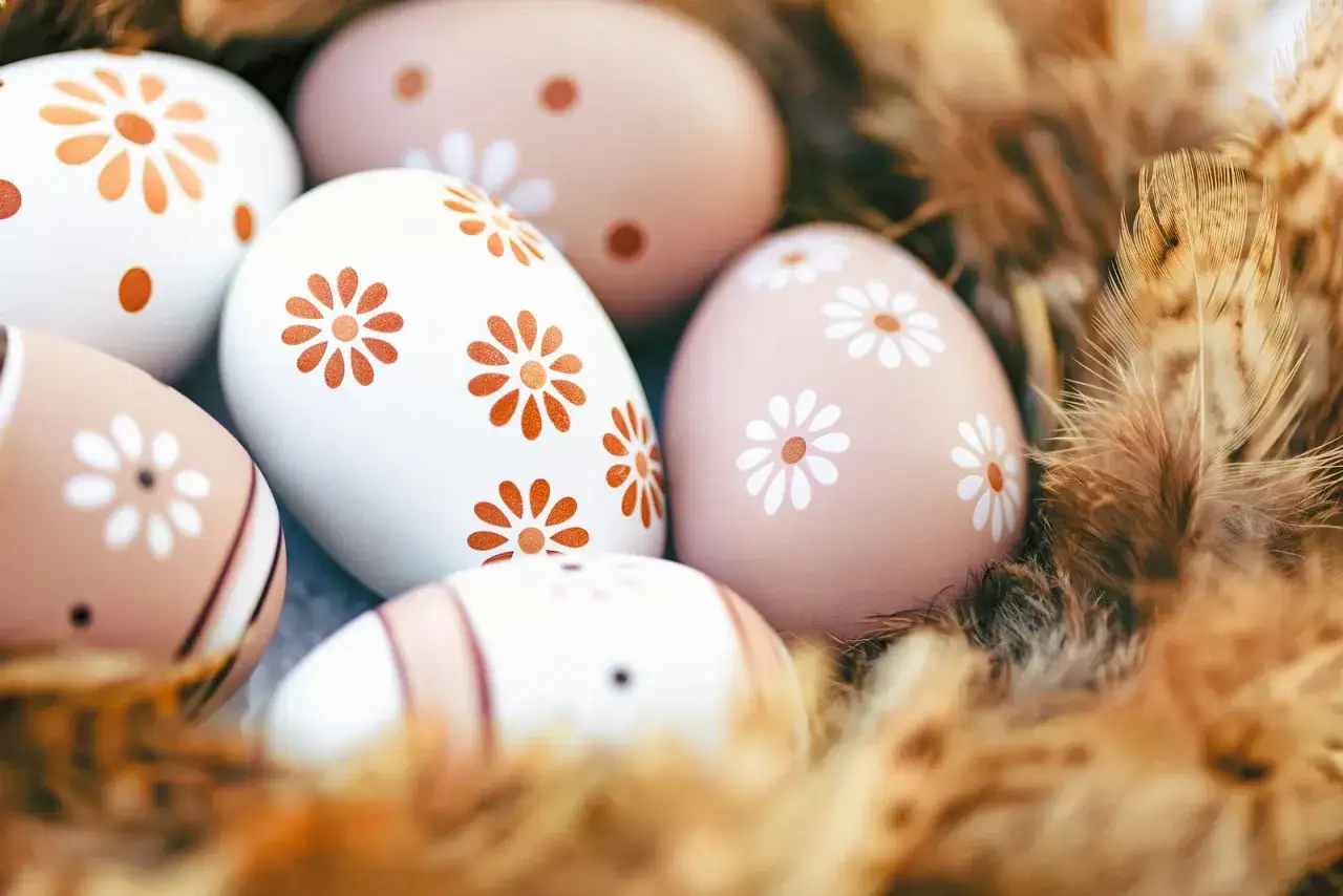 Ostereier mit Blumenmuster, einige braun, andere weiß, liegen in einem Nest aus Federn.
