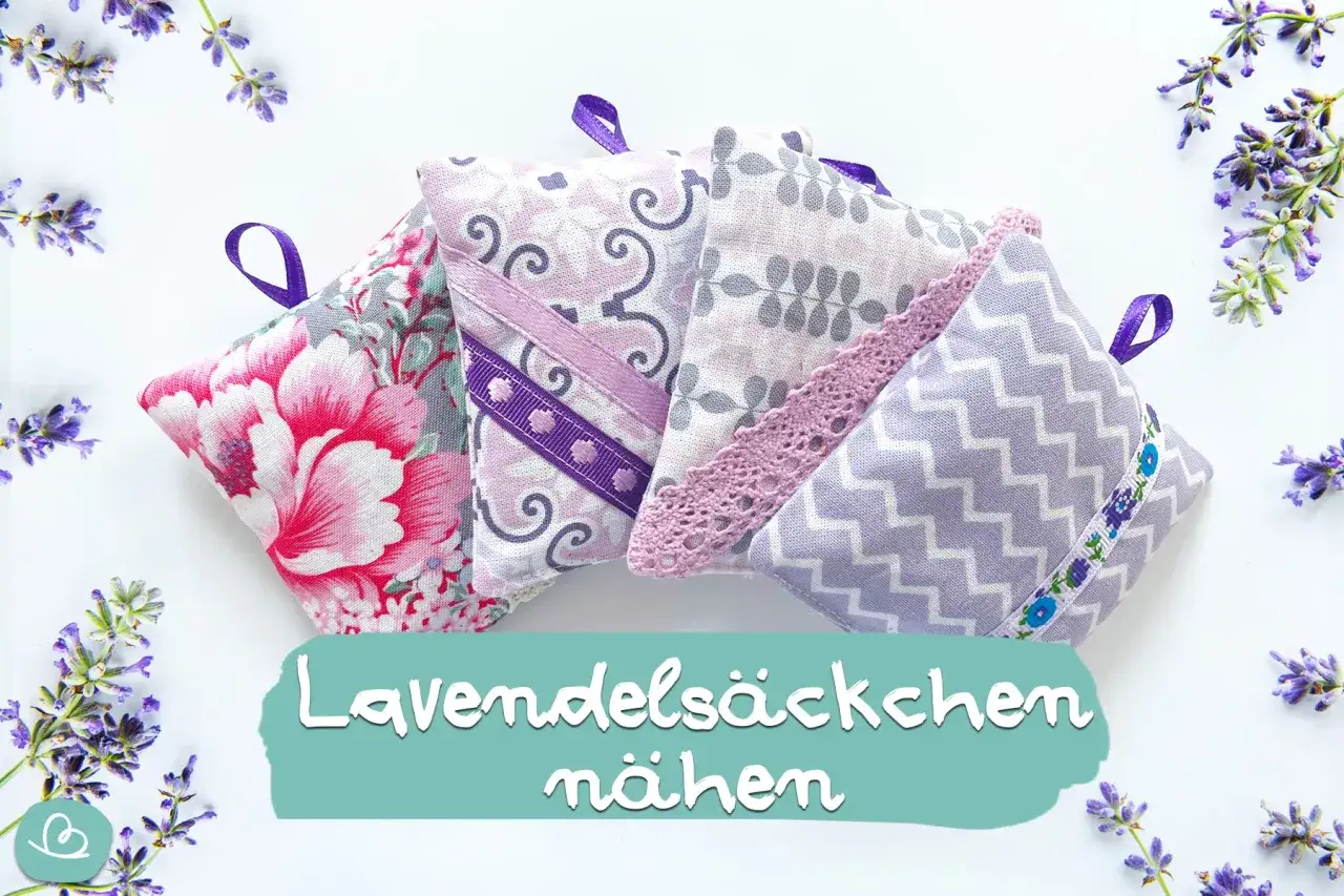 Vier selbstgemachte Duftkissen mit Lavendel-Motiven und B&auml;ndern, umgeben von frischen Lavendelzweigen.