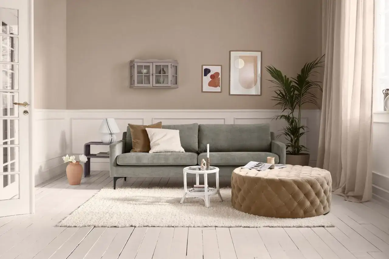 Gemütliches Wohnzimmer mit taupefarbener Wandfarbe, die tolle wandfarbe wohnzimmer ideen inspiriert. Ein graues Sofa, ein beiger Hocker und ein flauschiger Teppich laden zum Entspannen ein.