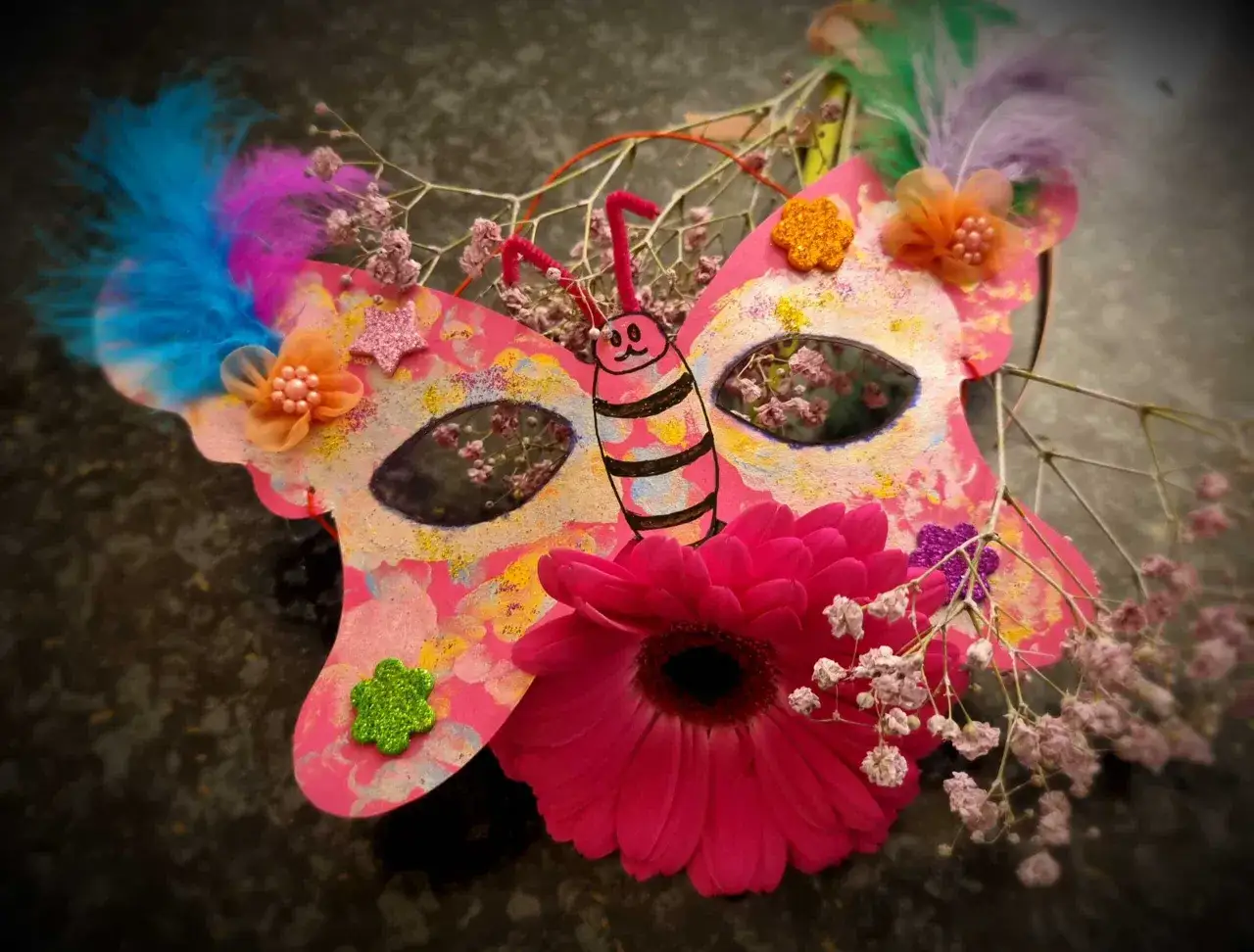 Bunte Schmetterlings-Faschingsmaske mit Federn, Blumen und Glitzer. Eine Vorlage zum Basteln für Karneval.