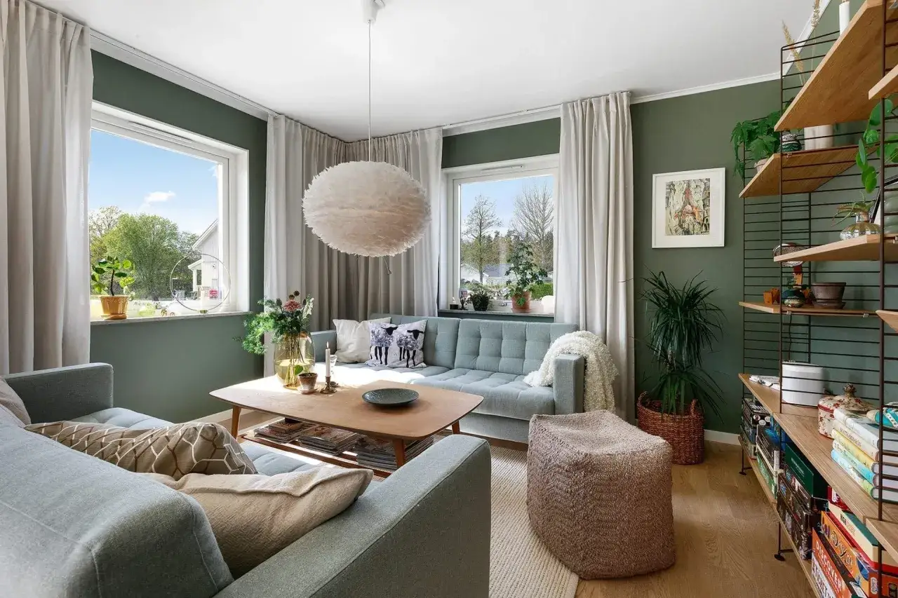 Gem&uuml;tliches Wohnzimmer mit vielen Pflanzen als Deko-Ideen. Helle Sofas, Holztisch und ein Feder-Pendelleuchte schaffen eine einladende Atmosph&auml;re.