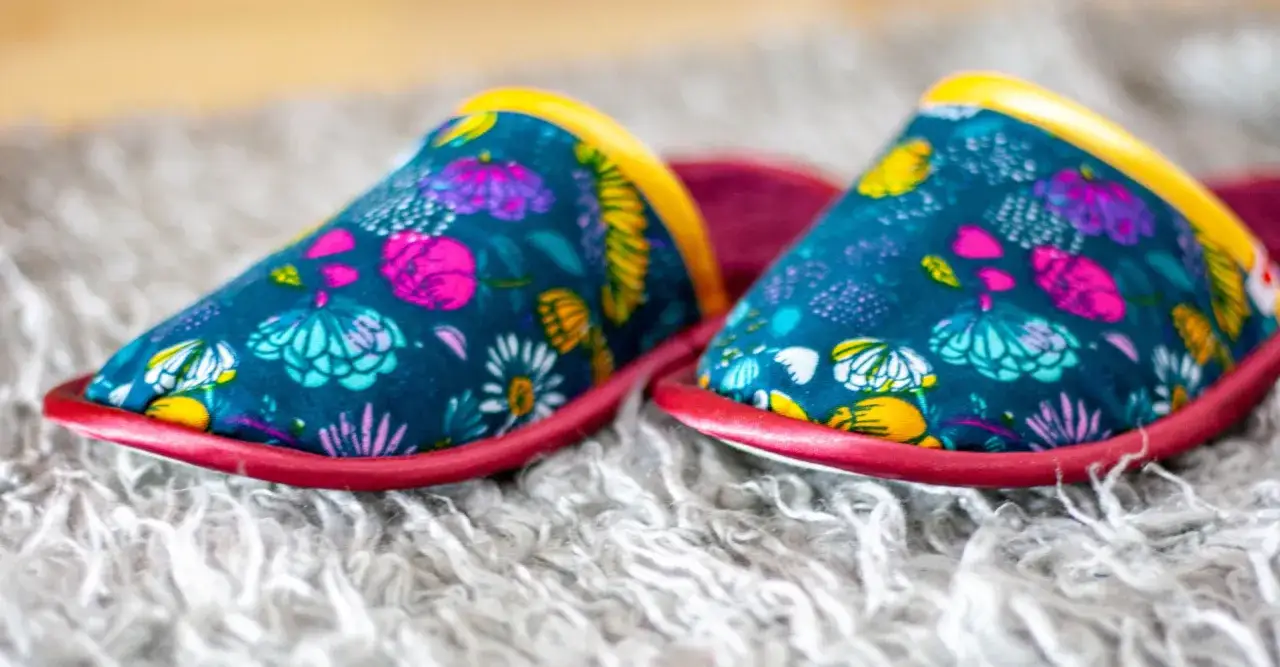 Bunte, selbstgemachte Hausschuhe mit Blumenmuster auf flauschigem Teppich.