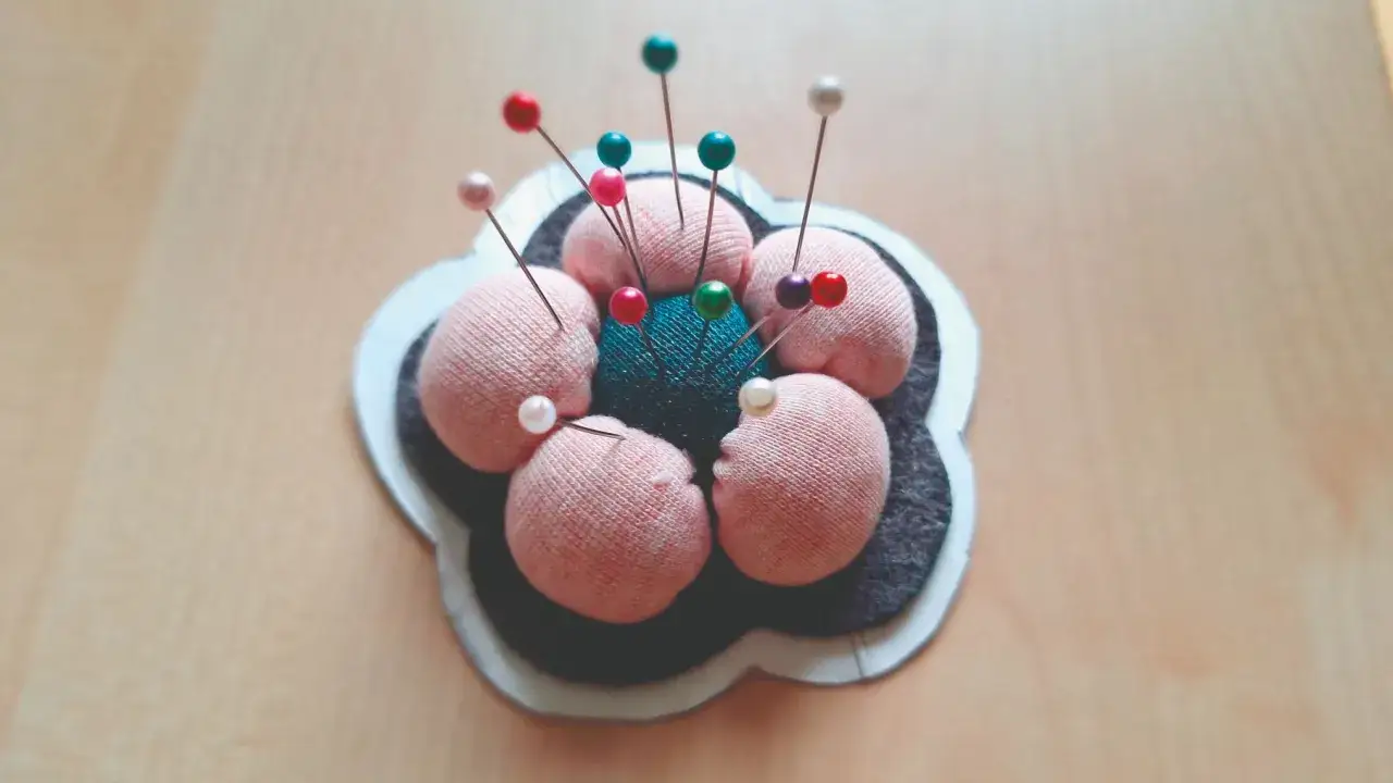 Ein selbstgemachtes Nadelkissen in Blumenform, mit rosa und t&uuml;rkisfarbenen Kugeln, best&uuml;ckt mit bunten Stecknadeln.
