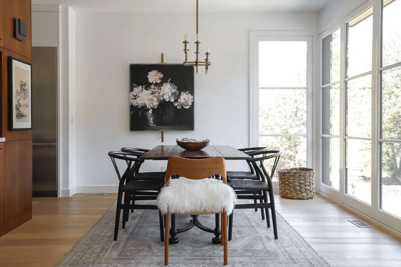 Ein stilvolles Esszimmer gestalten: Holztisch, schwarze Stühle, ein Kunstwerk mit Blumen und ein Teppich schaffen Gemütlichkeit.