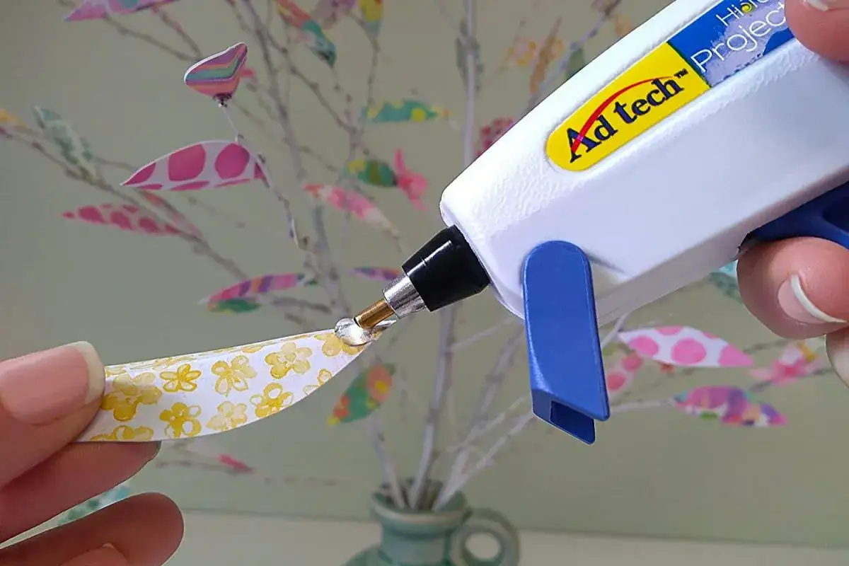 Hei&szlig;klebepistole tropft auf Papierblatt mit Blumenmuster. Perfekt, um bastelkleber selber machen.