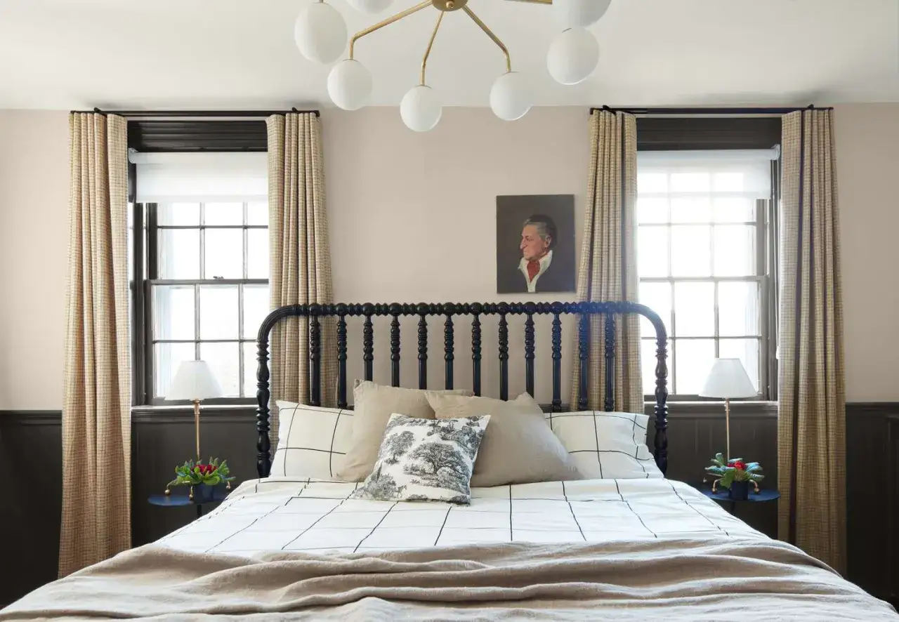 Gemütliche wandgestaltung mit warmen schlafzimmer farben. Ein Bett mit schwarzem Kopfteil, karierten Vorhängen und einem Porträt über dem Bett.